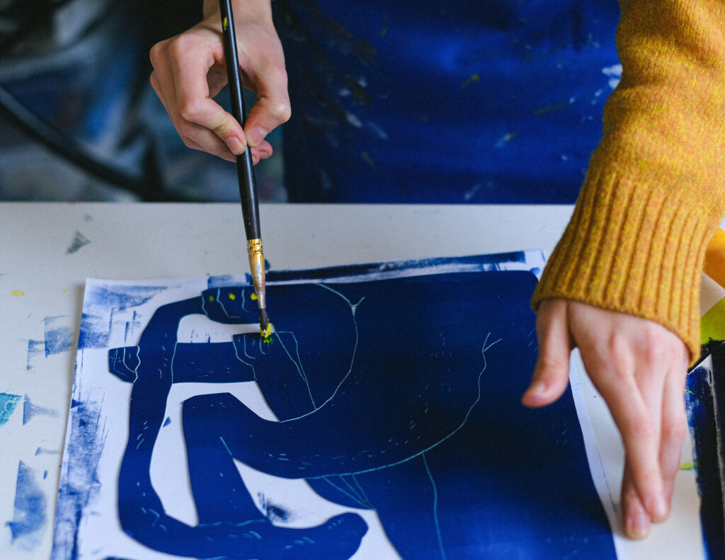 A person is painting on paper with blue paint.